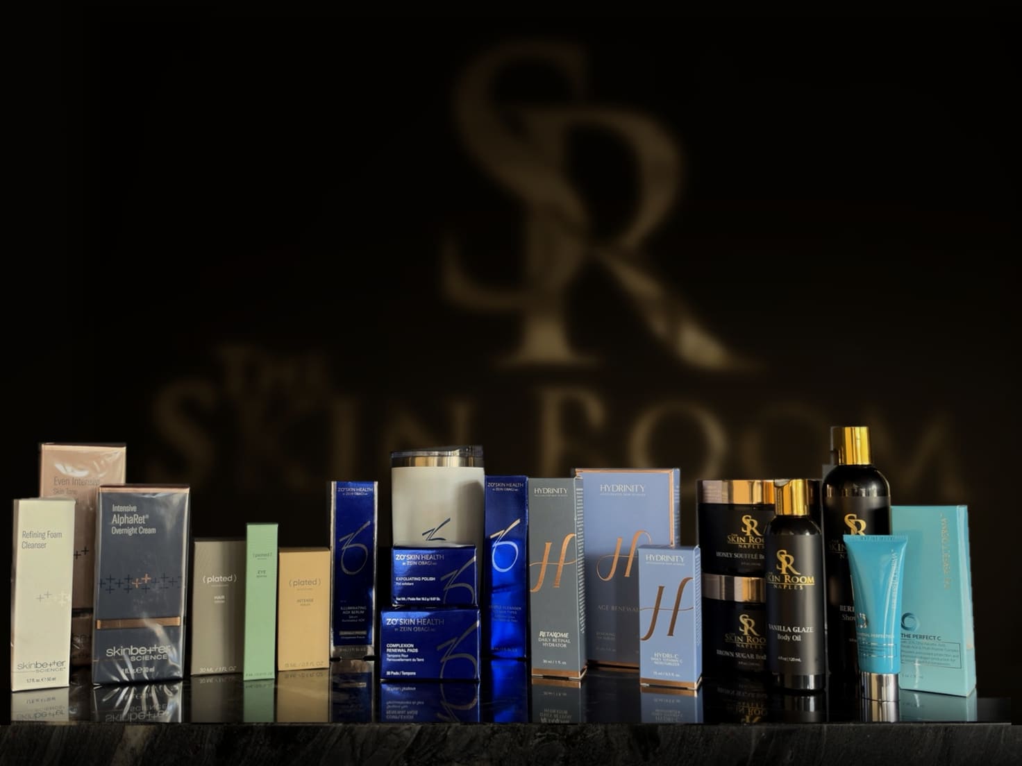 The giveaway prizes on our counter: skinbetter science, (plated) Skin Science, ZO Skin Health, Hydrinity, Body by The Skin Room and The Perfect Derma, with the gold SR logo on the wall behind